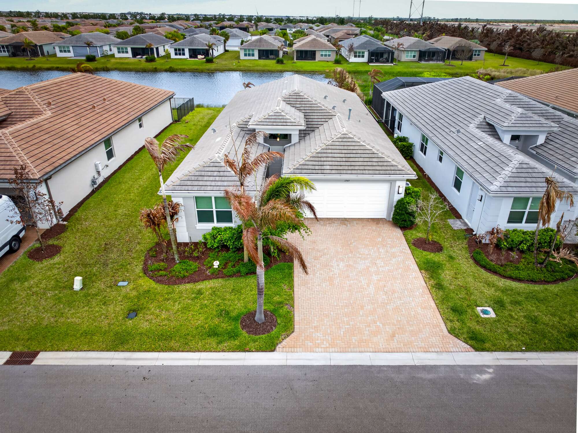 Aerial view of the home from the street, with the paver driveway and two-car garage in front and the lake immediately behind the house.