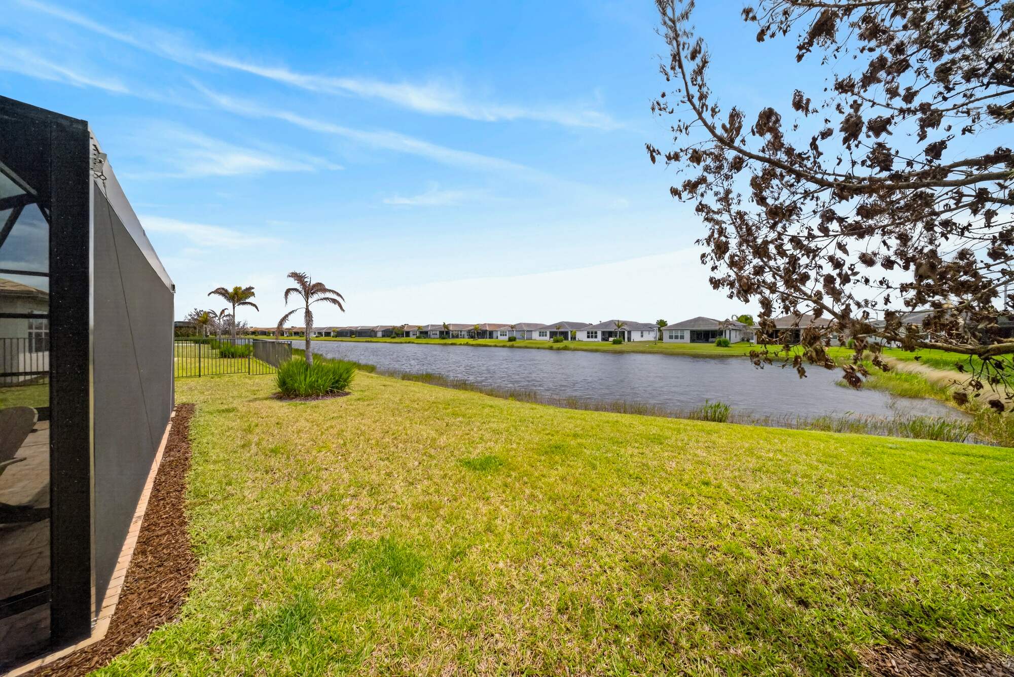 View across the back lawn from beside the screened lanai, looking out over the lake to the homes on the far shore.