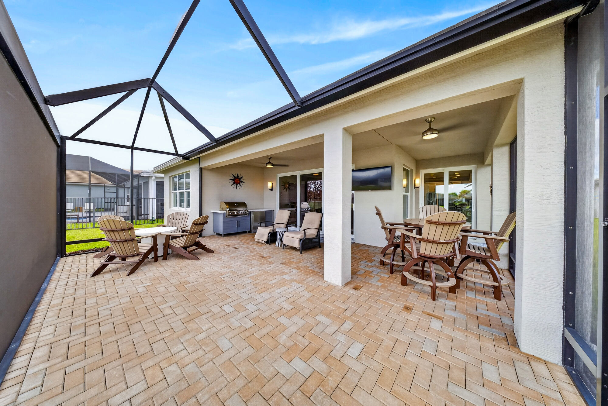 Second view of the screened lanai, showing the full extended paver patio, the outdoor kitchen and a mounted television under the covered section.