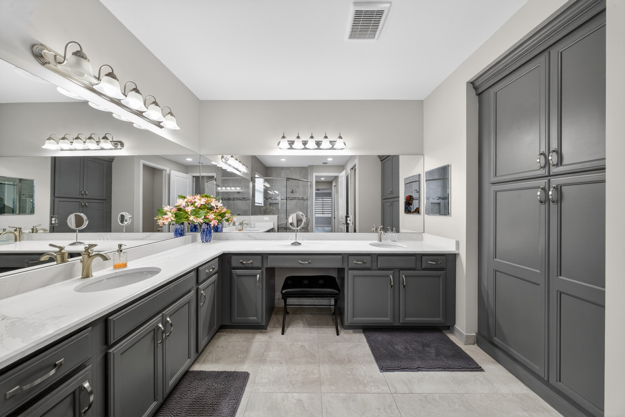 Primary bathroom with a double quartz vanity, a seated makeup station between the sinks, framed mirrors and a full-height linen cabinet.