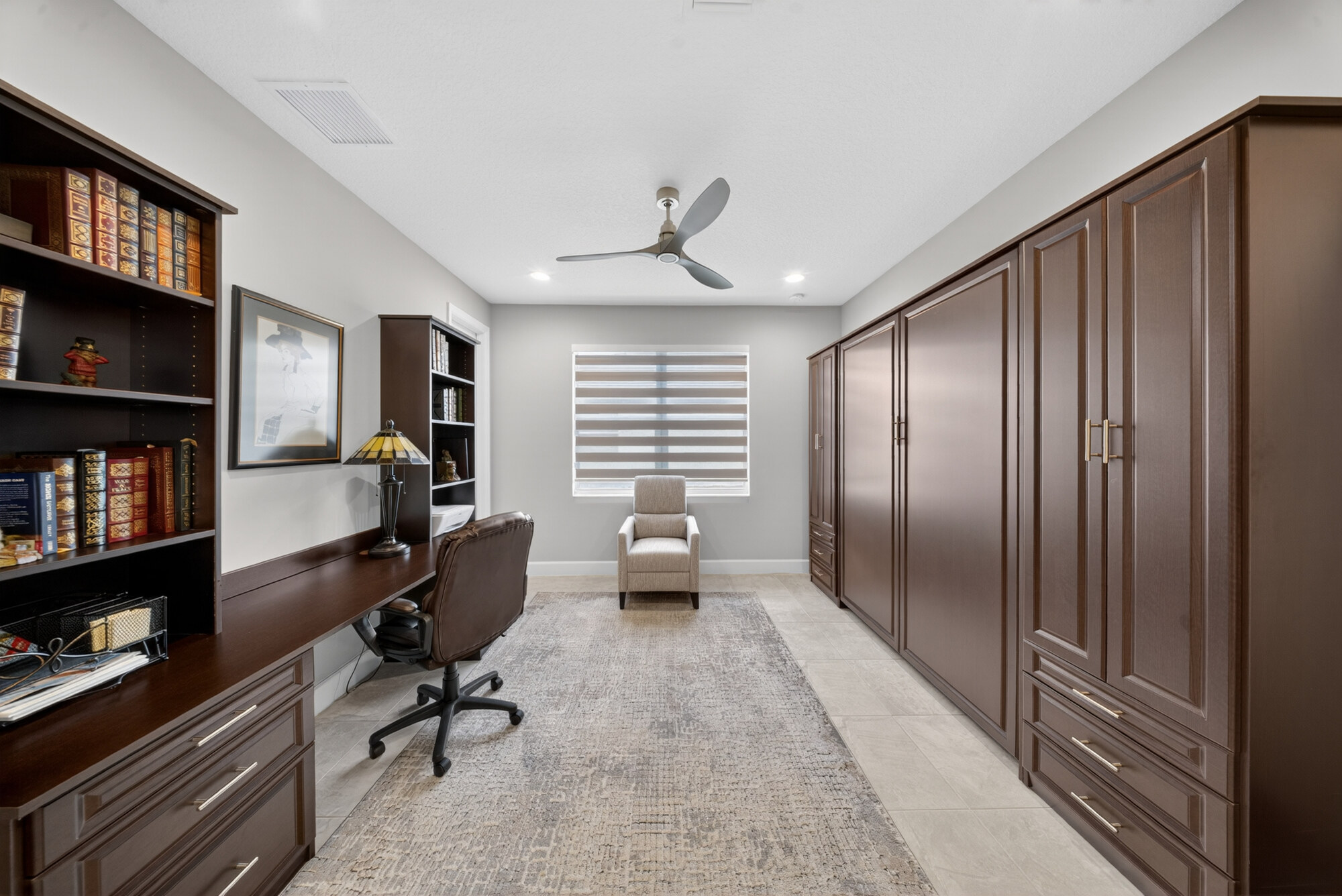 Den furnished as an office, with a built-in desk and bookshelves along one wall and full-height cabinetry along the other.