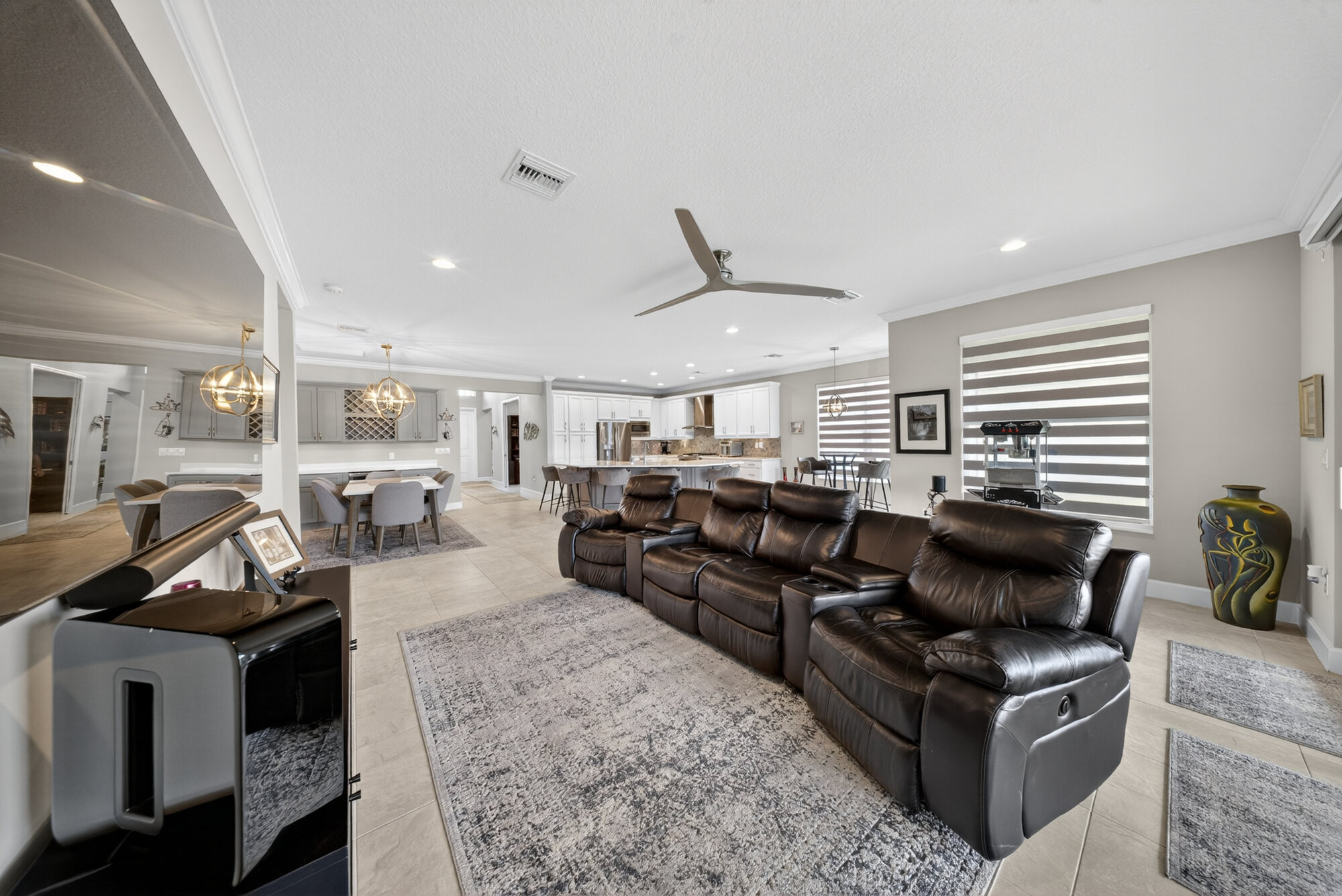 Open great room furnished with a leather reclining sectional on an area rug, looking through to the dining area and kitchen beyond.
