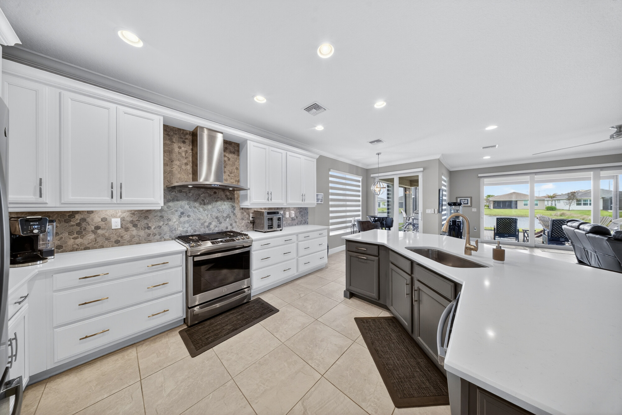 Kitchen with a large quartz island, stainless hood over the range, tile backsplash and sliding glass doors out to the lanai.