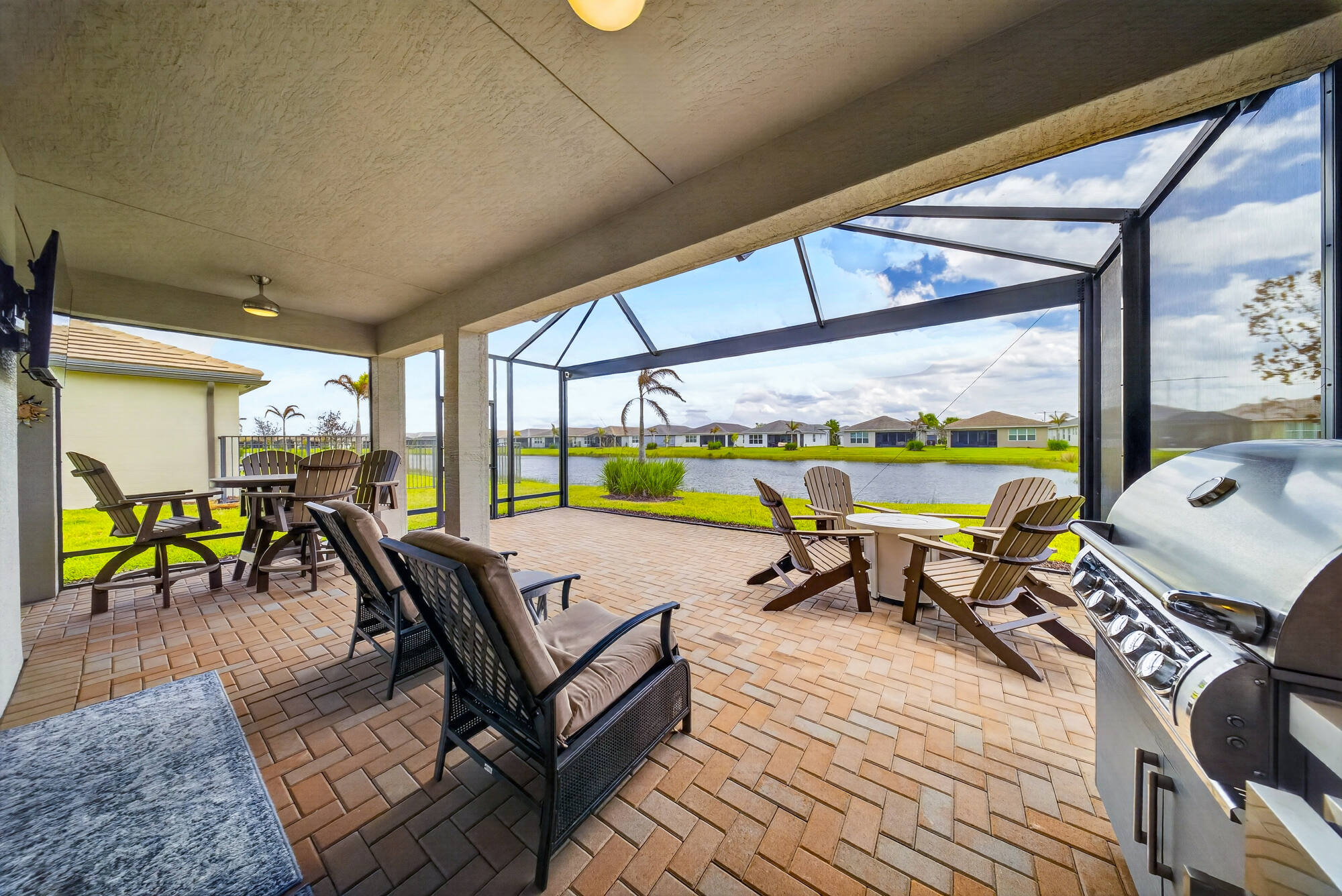 Covered lanai with a built-in grill and seating, opening onto the screened paver patio with the lake directly behind.